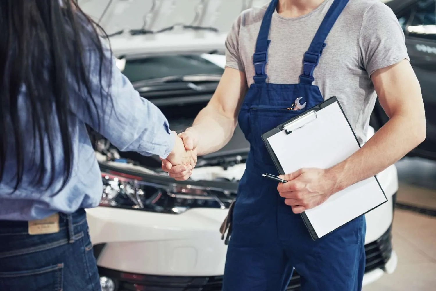 Mechanic with a clipboard shaking hands with a car owner